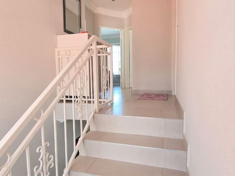 A bright hallway featuring a tiled staircase with a decorative wrought iron balustrade and classic ceiling cornicing.