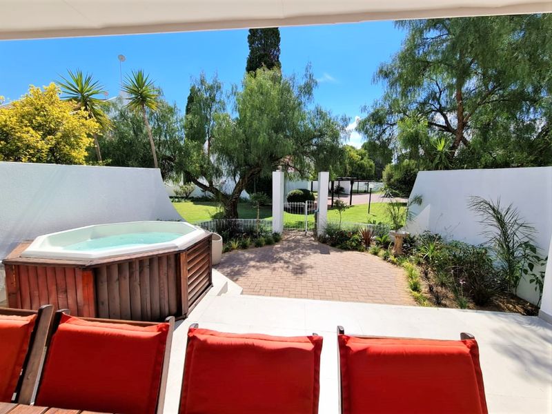 A covered patio area featuring a built-in hot tub, paved flooring, and direct access to a landscaped garden through a private gate.