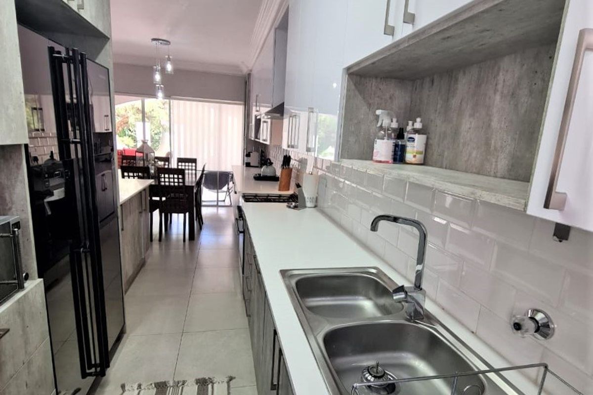 Modern galley-style kitchen featuring white cabinetry, stone countertops, subway tile backsplash, and integrated appliances, leading into an open-plan dining area.