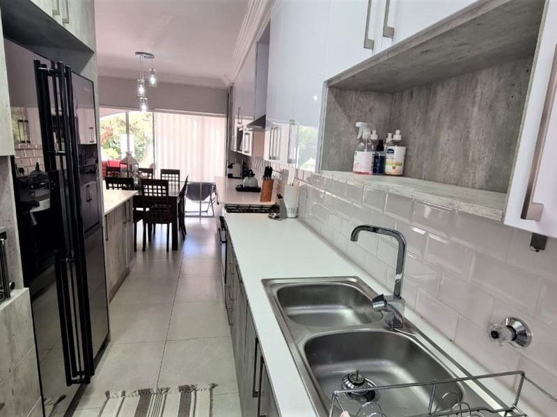Modern galley-style kitchen featuring white cabinetry, stone countertops, subway tile backsplash, and integrated appliances, leading into an open-plan dining area.