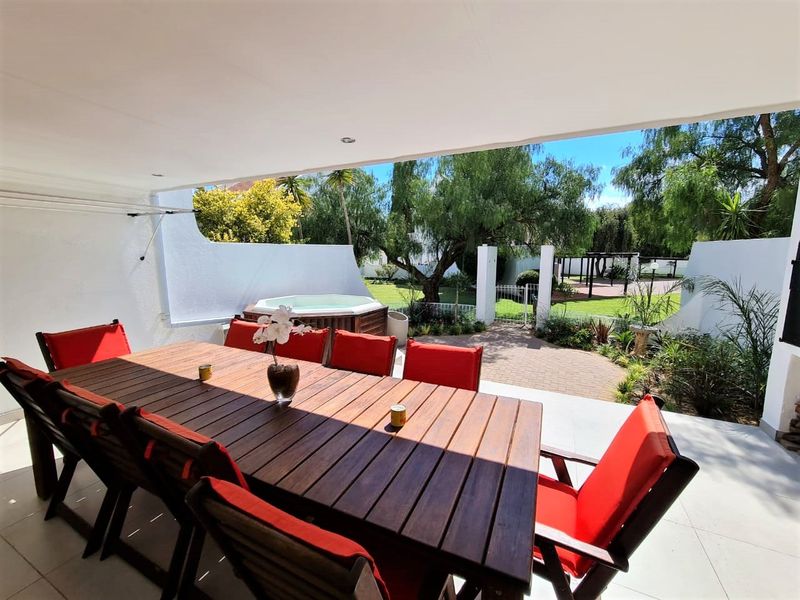 A spacious covered patio featuring tiled flooring and recessed lighting, overlooking a private garden area with a built-in spa and paved walkway.