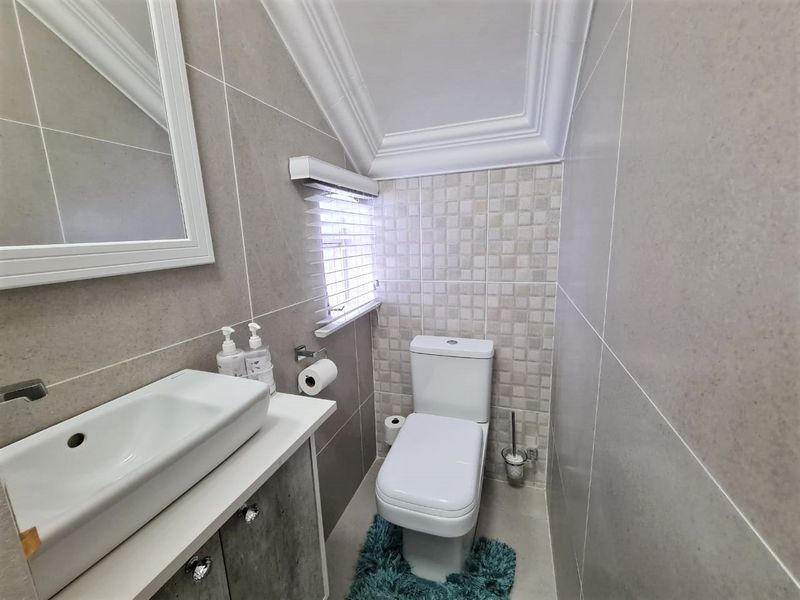 Compact modern bathroom featuring neutral wall tiles, a vessel sink vanity, and a white toilet under a sloped ceiling with crown molding.