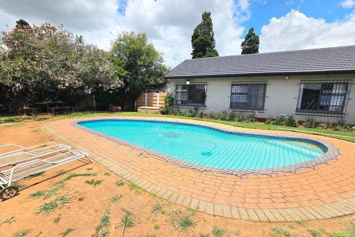 Outdoor pool area featuring a swimming pool with brick paving surround and a rear view of the house with security bars on windows.