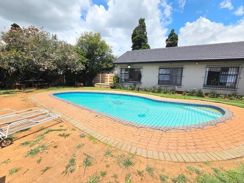 Outdoor pool area featuring a swimming pool with brick paving surround and a rear view of the house with security bars on windows.