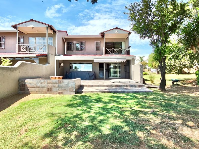 Rear view of the property featuring a paved patio area, built-in braai, and a spacious garden with mature trees.