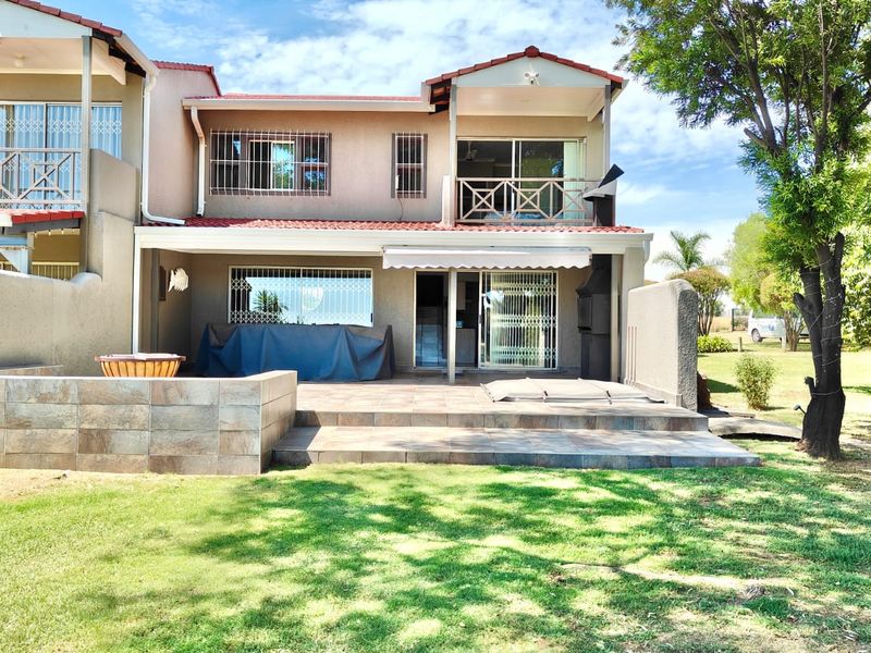 Rear view of the house featuring a tiled patio area, built-in braai, and an upper-level balcony overlooking the garden.