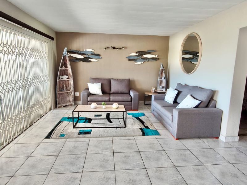 A bright living room featuring large sliding glass doors with security gates, neutral tiled flooring, and a feature wall.