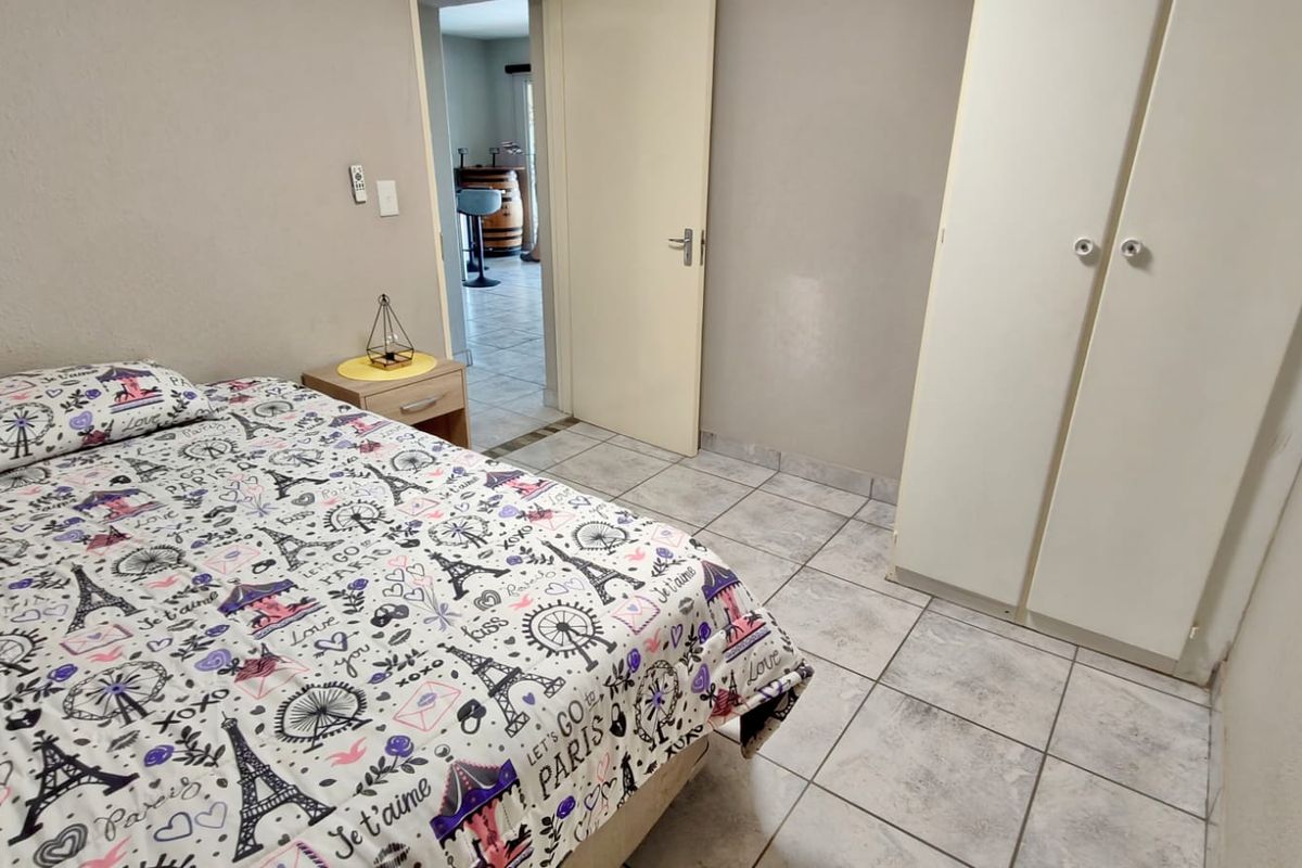 A bedroom featuring tiled flooring and built-in cupboards, with a doorway leading to an adjacent living area.