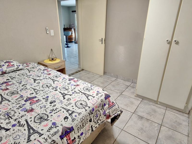 A bedroom featuring tiled flooring and built-in cupboards, with a doorway leading to an adjacent living area.