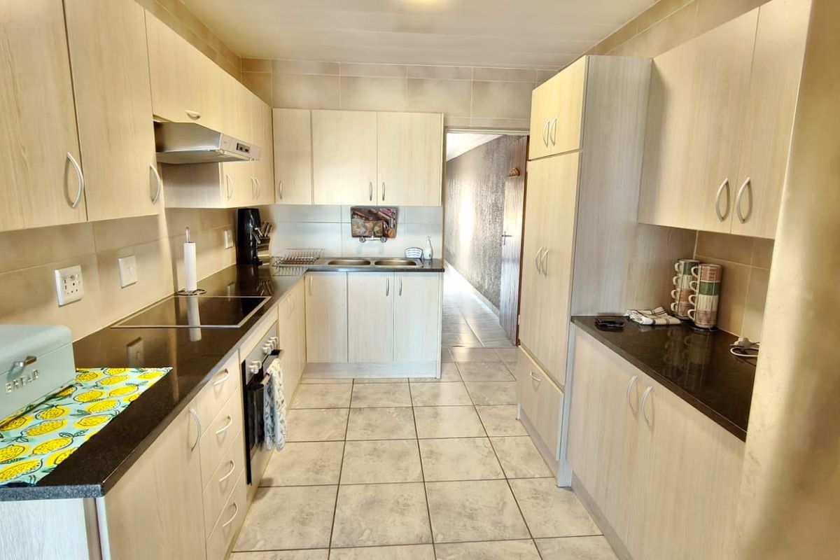 A functional kitchen featuring light wood-finish cabinetry, dark granite countertops, a built-in oven, hob, and extractor fan, complemented by neutral floor tiling.