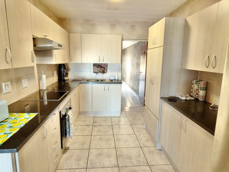 A functional kitchen featuring light wood-finish cabinetry, dark granite countertops, a built-in oven, hob, and extractor fan, complemented by neutral floor tiling.