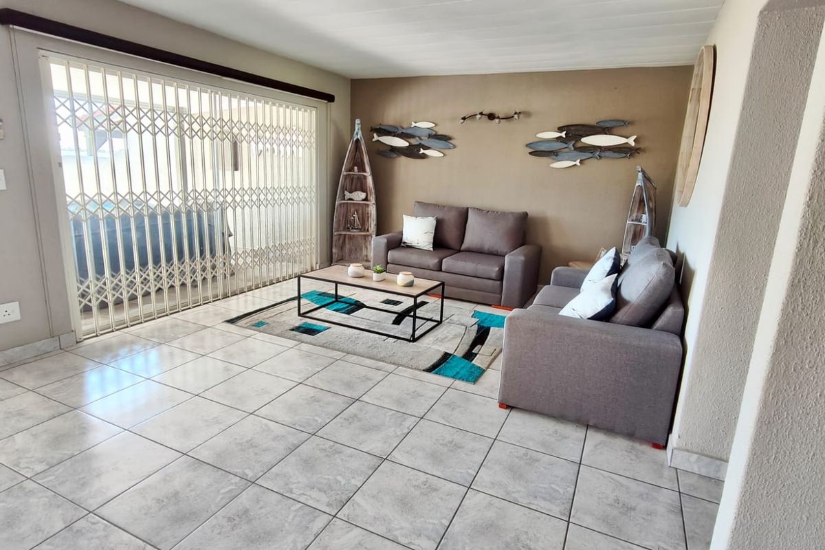 A living room featuring tiled flooring and a large sliding door with a security gate, providing access to the outdoor area.