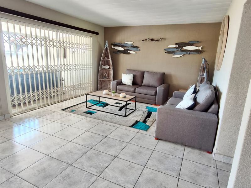 A living room featuring tiled flooring and a large sliding door with a security gate, providing access to the outdoor area.