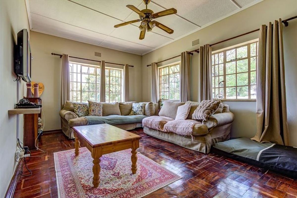 A cozy living room featuring classic parquet flooring, a ceiling fan, and large steel-framed windows that provide ample natural light.