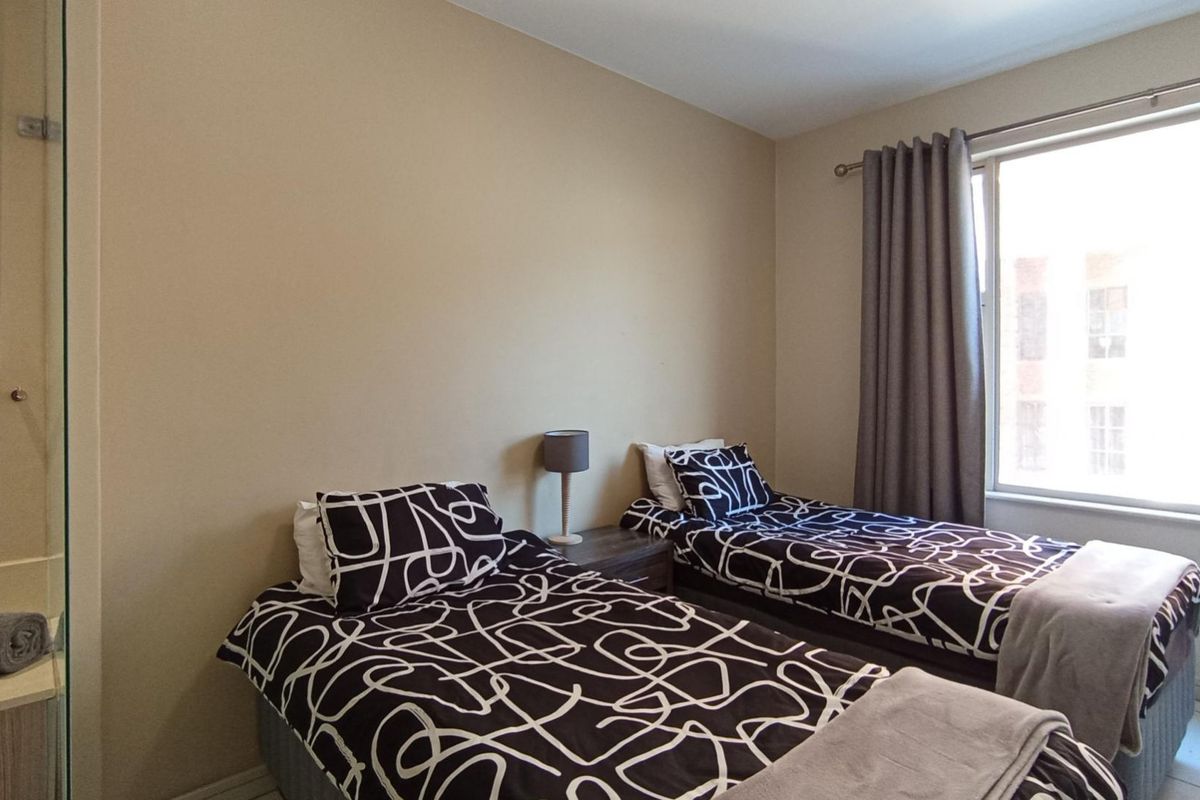 A functional bedroom featuring tiled flooring and a large window with curtain rails, providing natural light and a neutral color palette.