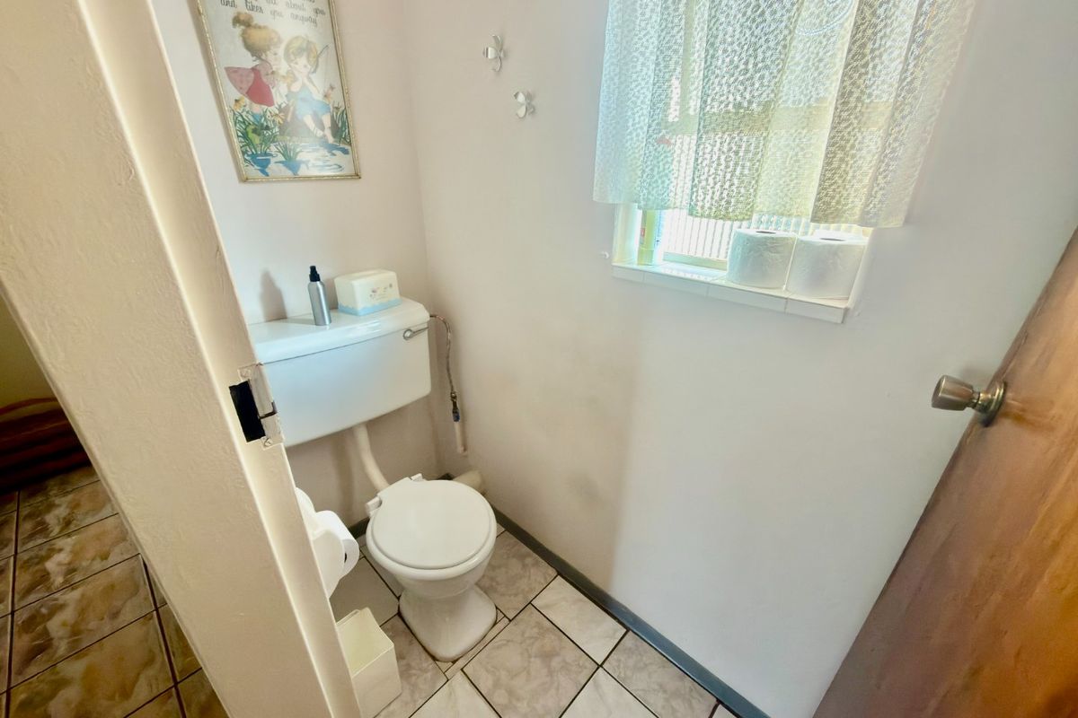 A compact bathroom featuring ceramic floor tiles, a standard flush toilet, and a window with natural light.