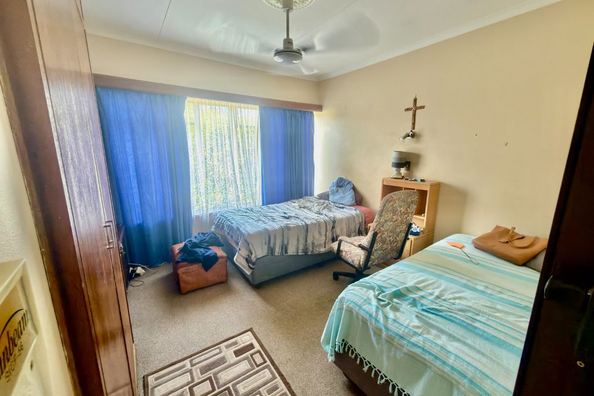 A bedroom featuring a built-in wardrobe, ceiling fan with decorative rose, and carpeted flooring. The space requires cosmetic updates to improve its overall condition.