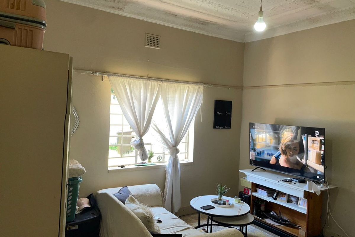 A living room featuring a classic pressed metal ceiling, picture rails, and security bars on the window, requiring cosmetic updates to improve its condition.