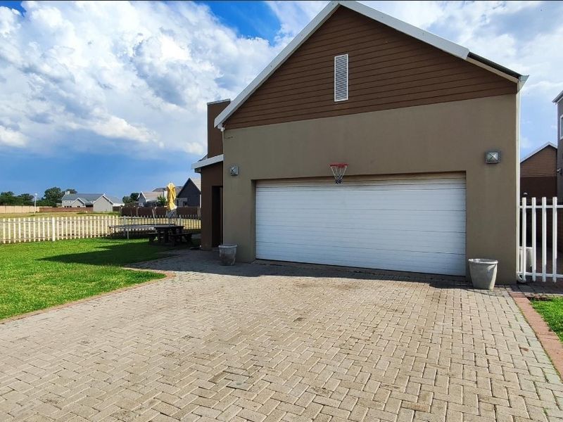 Exterior view of the property featuring a paved driveway, double garage, and a well-maintained lawn with perimeter fencing.