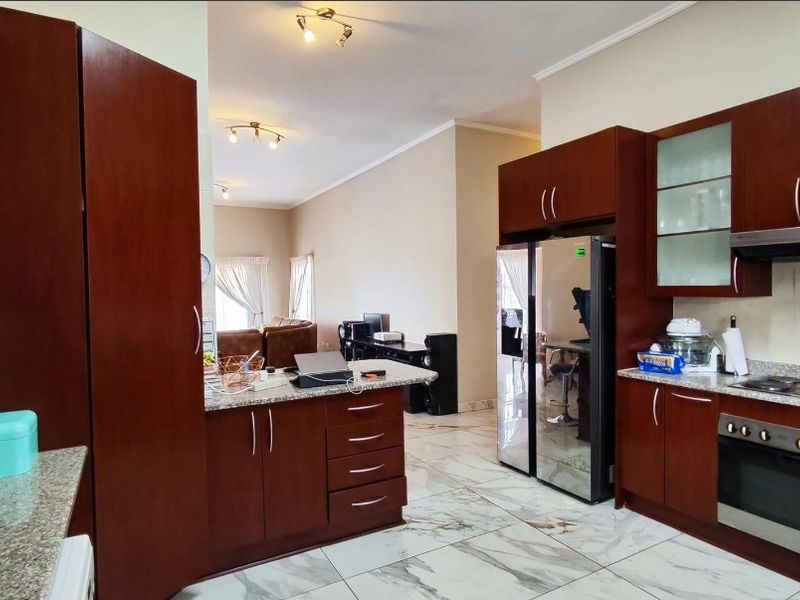 Open-plan kitchen featuring dark wood cabinetry, granite countertops, built-in oven, hob, and extractor fan, with marble-look floor tiles throughout the living area.