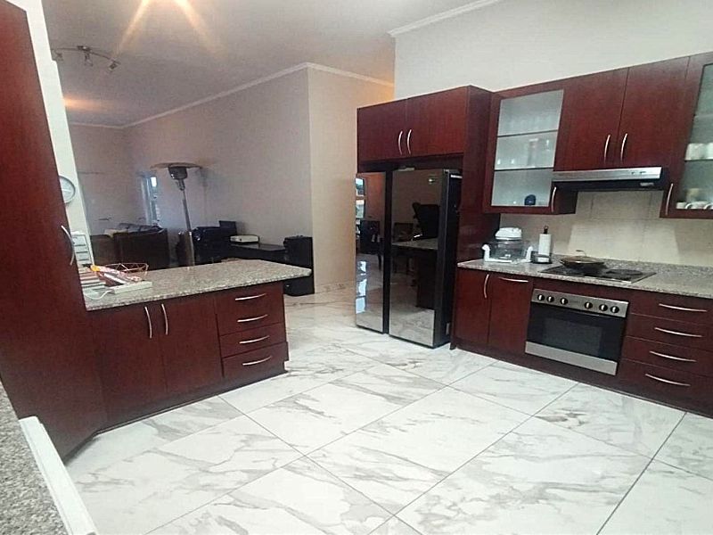 Open-plan kitchen featuring dark wood cabinetry, granite countertops, built-in oven, hob, and extractor fan, with large format marble-look floor tiles.