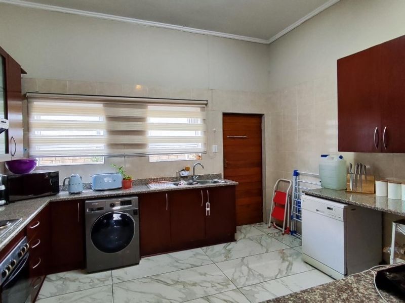 A functional kitchen featuring dark wood cabinetry, granite countertops, tiled flooring, and integrated space for laundry and dishwashing appliances.