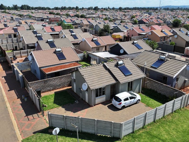 Aerial view of a residential property featuring a tiled roof with a solar water heater, a paved driveway, and a precast concrete boundary wall.