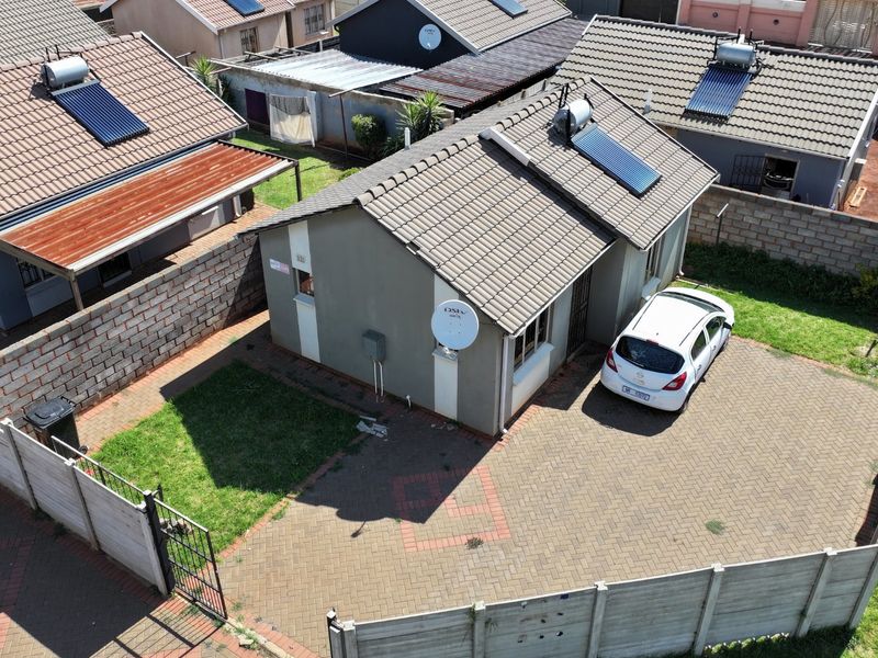 Aerial view of a residential property featuring a tiled roof with solar water heating, a paved driveway, and perimeter precast walling.
