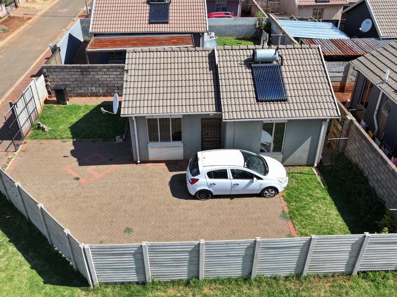 Aerial view of a residential property featuring a tiled roof with a solar water heater, paved driveway, and secure perimeter walling.