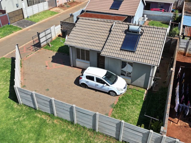 Aerial view of a residential property featuring a tiled roof with a solar water heater, paved driveway, and secure perimeter walling.