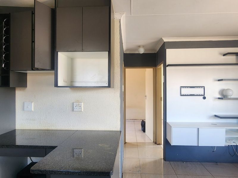 Open plan living area featuring dark cabinetry, granite countertops, and a built-in wall unit with neutral tiled flooring throughout.