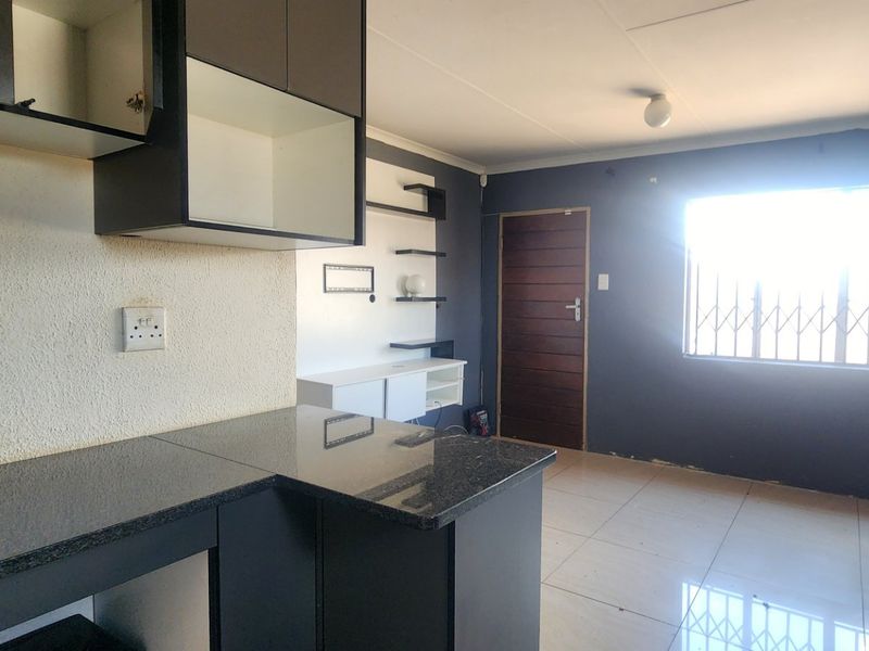 Open plan living area featuring tiled floors, granite kitchen countertops, built-in cabinetry, and a secure window with a metal security gate.