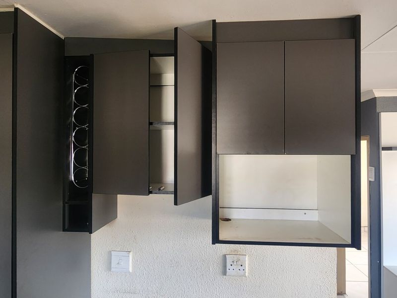A kitchen area featuring dark grey built-in cabinetry, including a wine rack and dedicated microwave shelf, set against a textured wall.