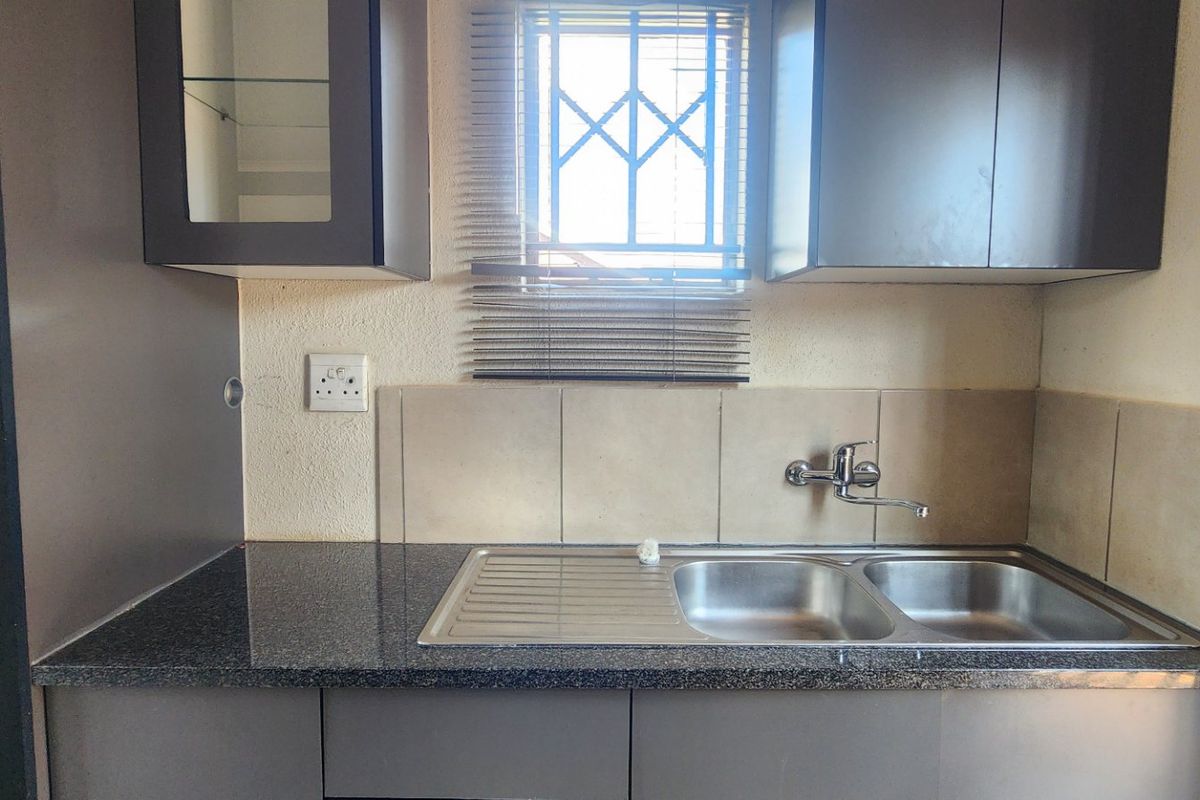 A compact kitchen area featuring dark cabinetry, granite countertops, a double bowl stainless steel sink, and a tiled splashback.