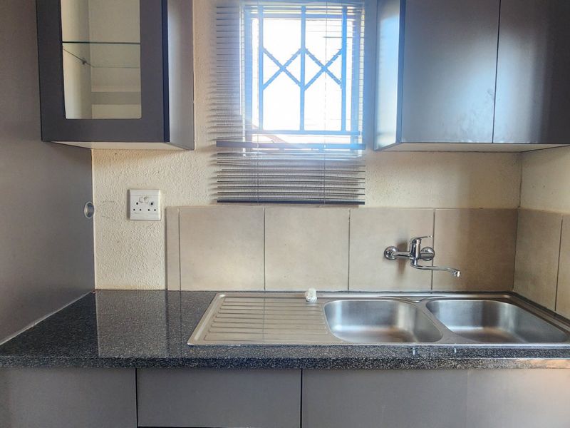 A compact kitchen area featuring dark cabinetry, granite countertops, a double bowl stainless steel sink, and a tiled splashback.