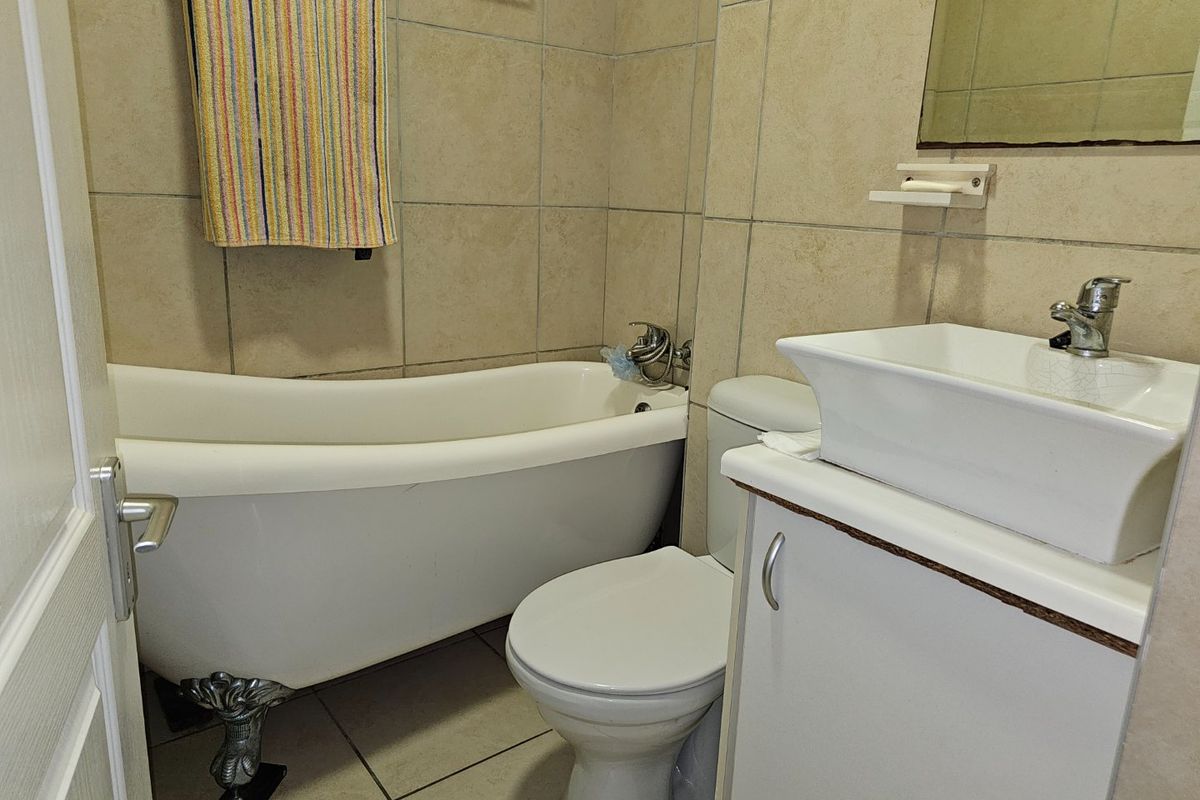 A compact bathroom featuring a clawfoot bathtub, a ceramic basin with vanity cabinet, and neutral wall tiling.