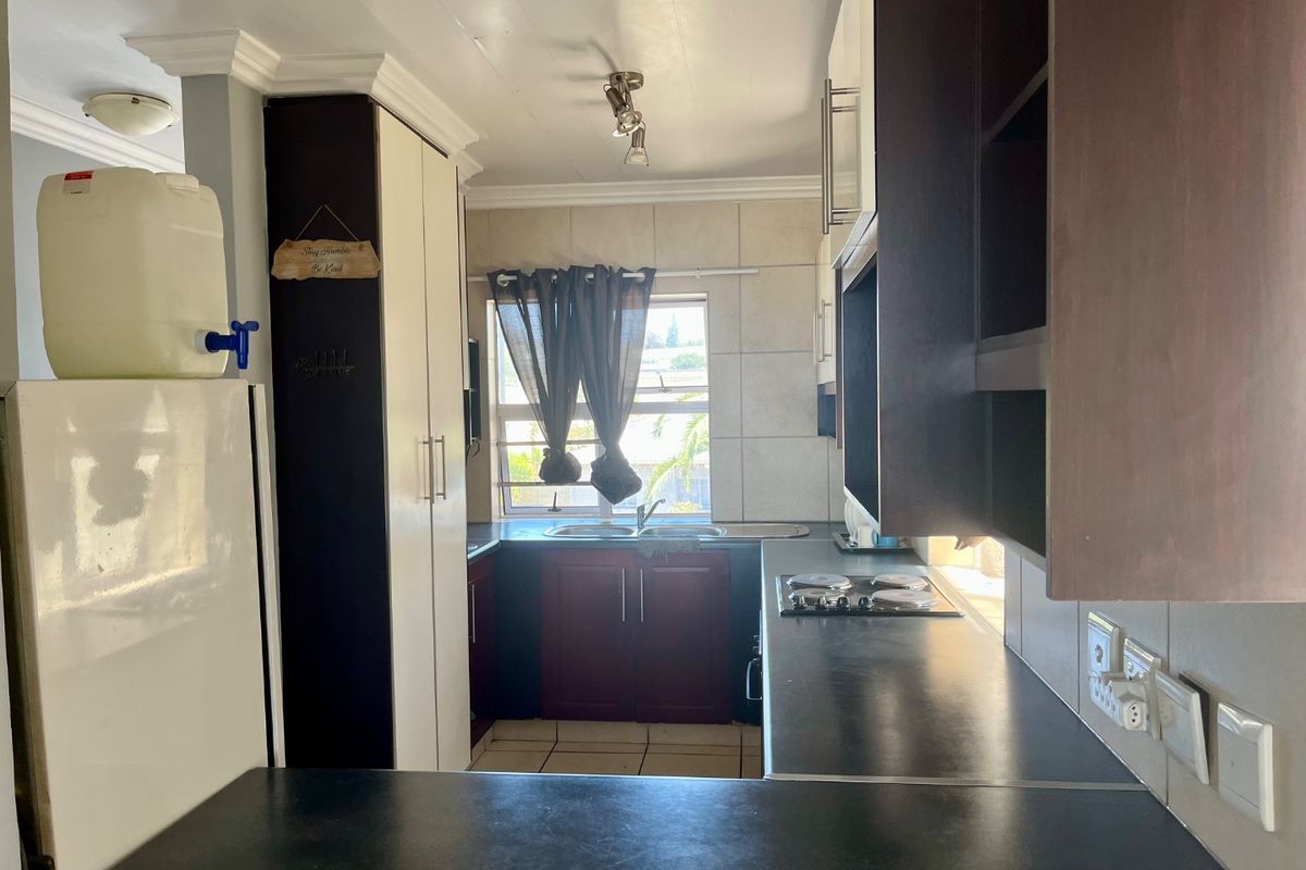 A functional kitchen featuring built-in cabinetry, dark laminate countertops, a stainless steel sink, and a built-in hob with tiled backsplash.