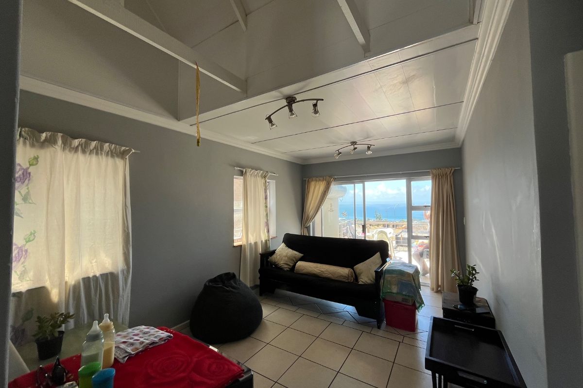 A living room featuring vaulted ceilings with exposed rafters, tiled flooring, and a sliding glass door providing access to a balcony with ocean views.