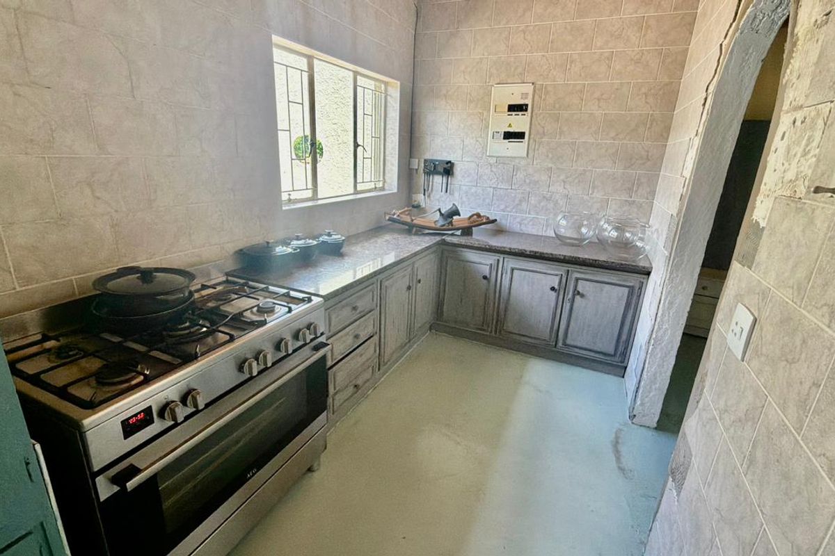 A functional kitchen featuring a gas stove, built-in cabinetry, and tiled walls, currently requiring cosmetic updates and finishing to the surrounding wall structures.