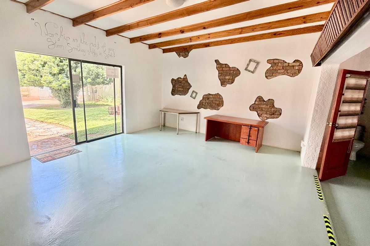 Spacious living area featuring exposed timber ceiling beams, painted concrete floors, and large sliding glass doors providing direct access to the garden.