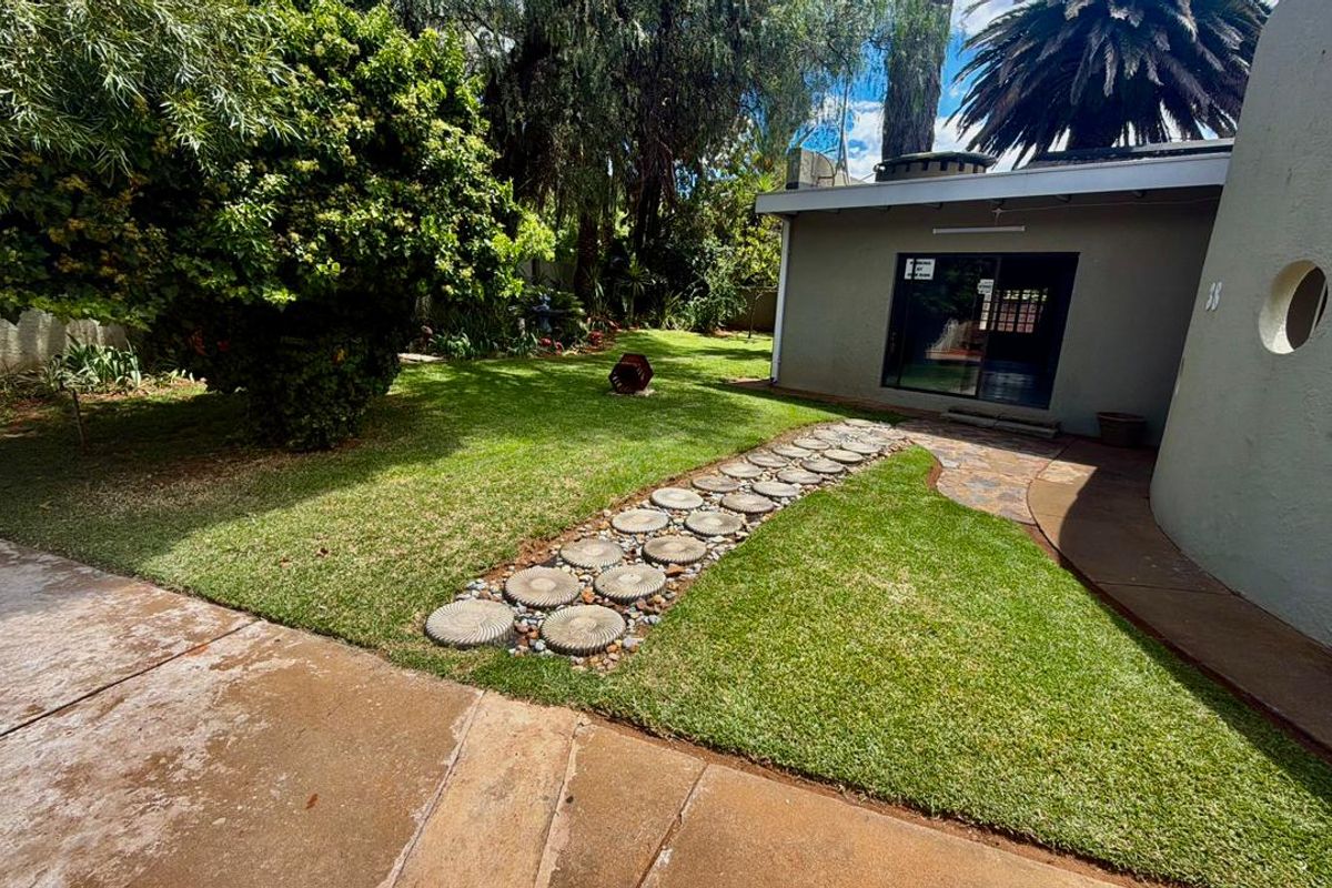 A well-maintained rear garden featuring a lush lawn, decorative concrete stepping stones, and a sliding glass door providing access to the home.