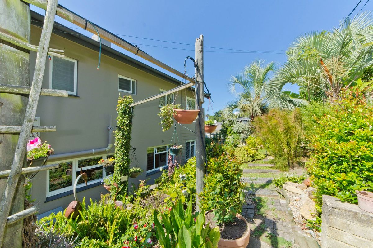 A view of the rear exterior of the house featuring a landscaped garden, stone pathway, and established greenery.