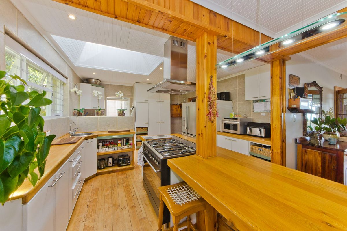 A well-lit kitchen featuring timber cabinetry, a gas stove with stainless steel extractor, a timber breakfast bar, and a bright skylight.