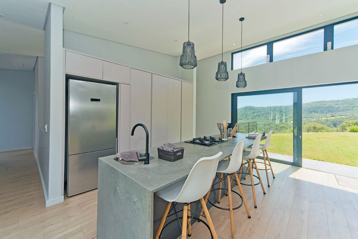 Modern open-plan kitchen featuring a stone-topped island with integrated gas hob, matte black faucet, and sleek cabinetry, overlooking a scenic landscape through large glass doors.