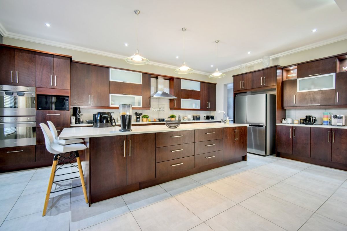 Modern kitchen featuring dark wood cabinetry, a large central island with stone countertops, integrated appliances, and contemporary pendant lighting.