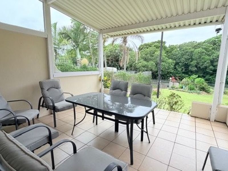 A covered patio area featuring tiled flooring and a built-in planter box, overlooking a lush garden setting.
