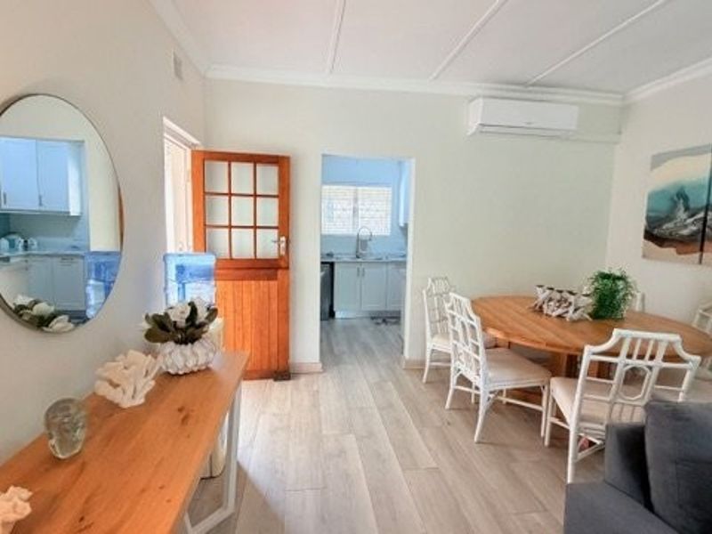 An open-plan living and dining area featuring light-toned laminate flooring, a split-system air conditioner, and direct access to the kitchen.