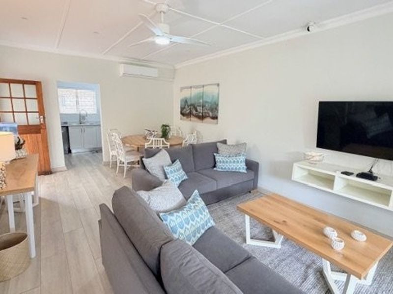 An open-plan living and dining area featuring tiled flooring, a ceiling fan, split-system air conditioning, and a wall-mounted floating media console.