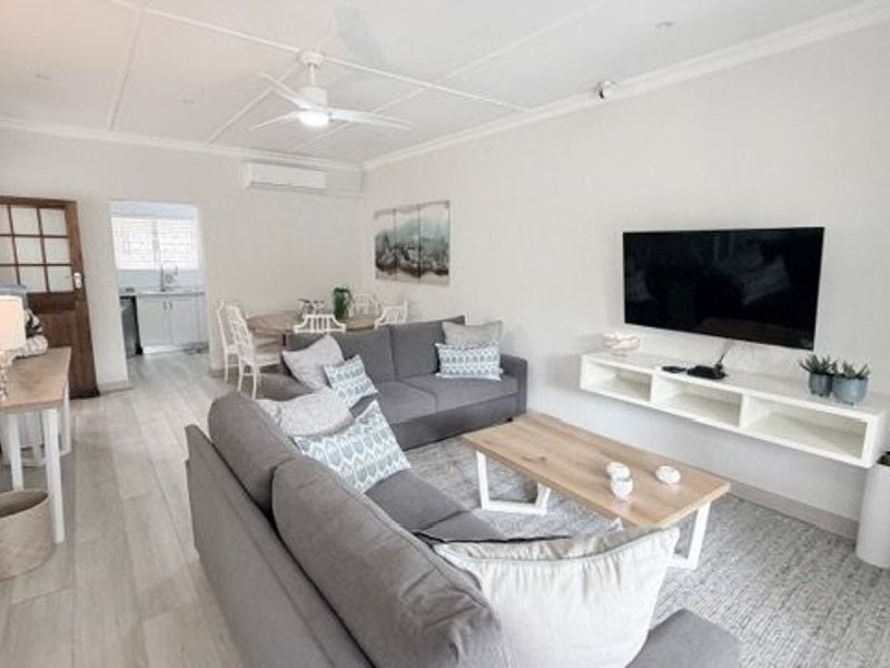 Bright open-plan living area featuring tiled floors, a ceiling fan, split-system air conditioning, and a modern floating media console.