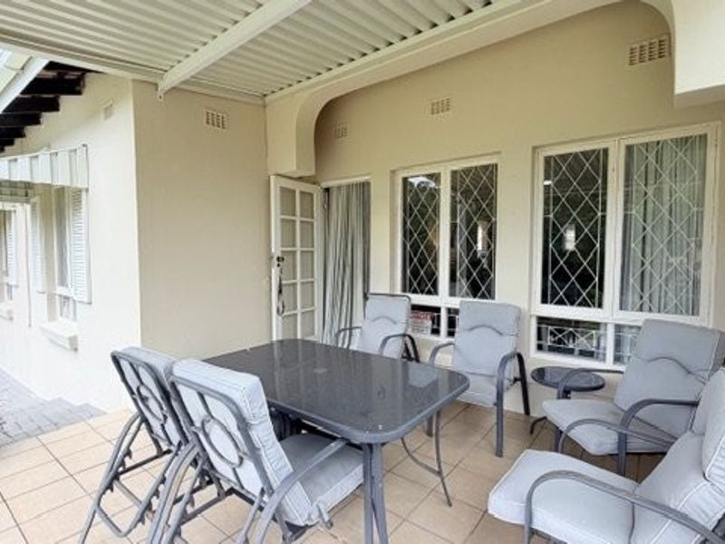A covered patio area featuring tiled flooring, security-barred windows, and direct access to the home through a classic french door.